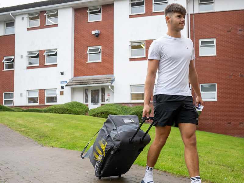 A student pulling a suitcase along a path, heading towards his student accommodation.
