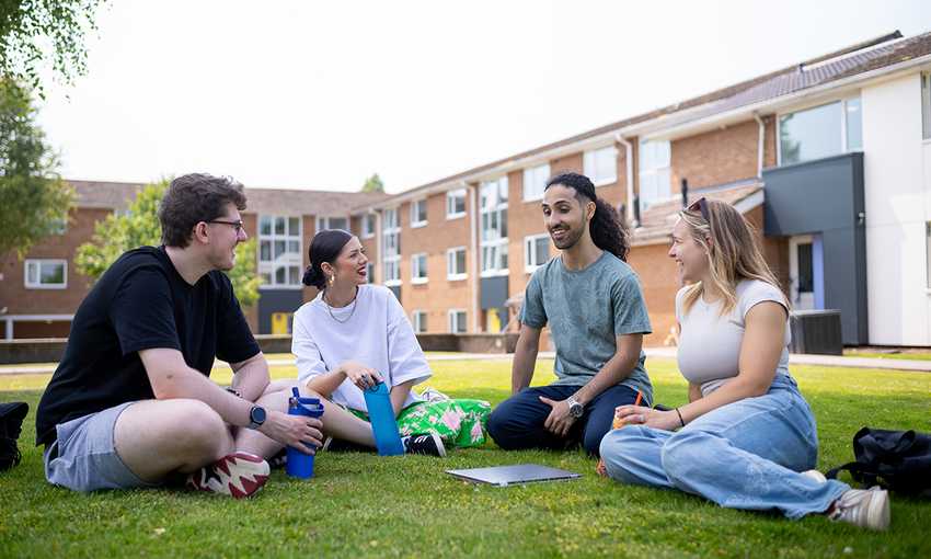 Group of four students sitting on the grass, chatting and laughing outside a student accommodation building