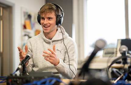 Alex Hyman, wearing headphones, talking with someone out of view