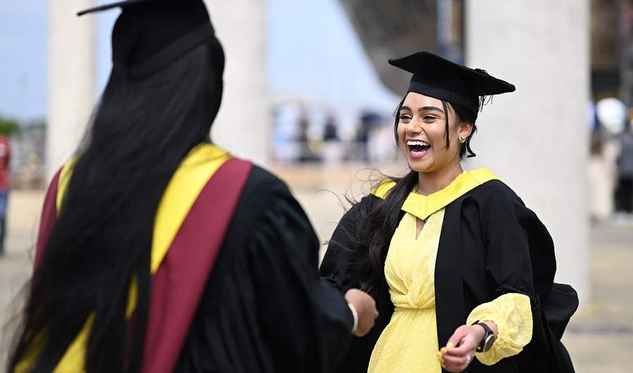 Two women in graduation gowns, celebrating their academic achievements with smiles and camaraderie.