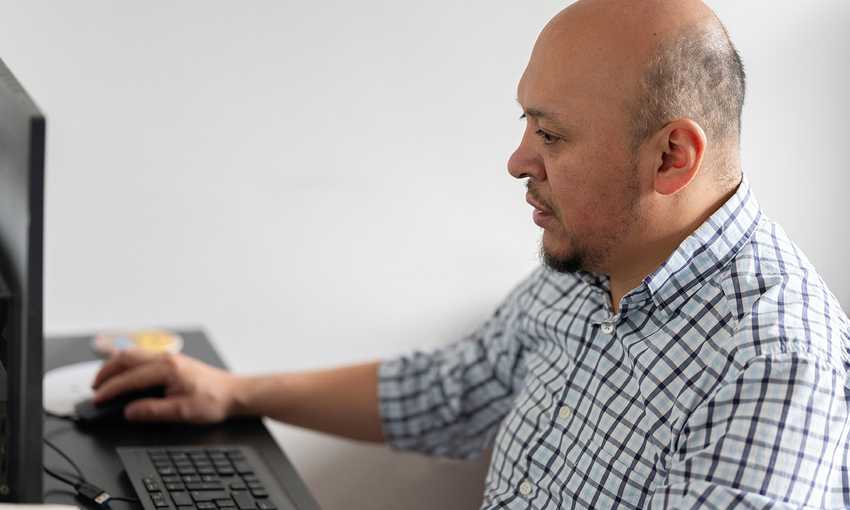 A man seated at a desk, focused on his work while using a computer.