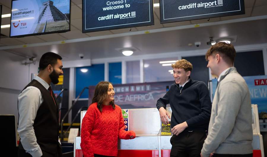 A group of people stand together talking next to an airport check-in desk.
