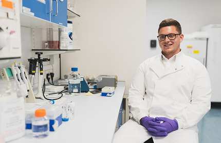 Ben Stevens in lab coat and gloves sat at a workstation