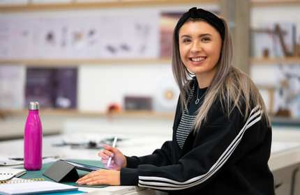 A person sits at a table holding a stylus in their hand. In front of them is a drawing tablet.