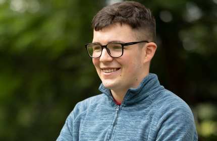 A person with glasses. In the background are some trees.