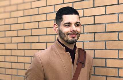 Beau Fryers, wearing a brown overcoat, stands in front of a light-coloured brick wall