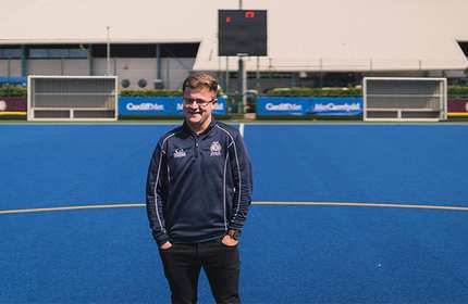 Ben Holdaway, in Cardiff Met branded tracksuit, stands on an artificial blue sports field