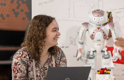 Charlotte Hale smiles as she looks towards a colleague working on a small humanoid robot