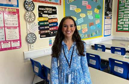 Chloe Davies stands at the back of a classroom and in front of classroom displays