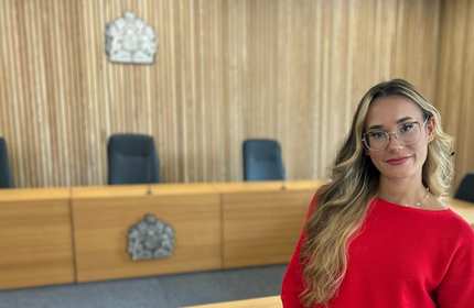 Ema Nata stands in front of a row of desk branded with the United Kingdom coat of arms
