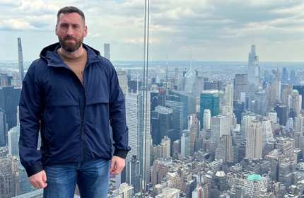 Gary Hewitt stands in front of a glass fence overlooking the New York City skyline