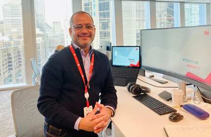 Jude Labonte stands leaning on a sit-stand work desk in an office overlooking a city
