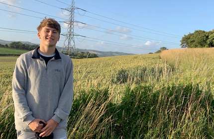 Louis Jones, wearing a grey top, stands in front of a sunny wheat field