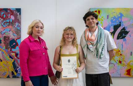 Three people pose for a photo. The person in the middle is holding a certificate.