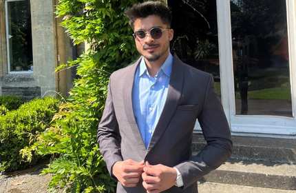 Vartesh Kumar, wearing a blue shirt and sunglasses, buttons his suit jacket