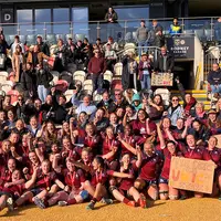 A collective of women in maroon shirts raises a sign, demonstrating camaraderie and shared goals.