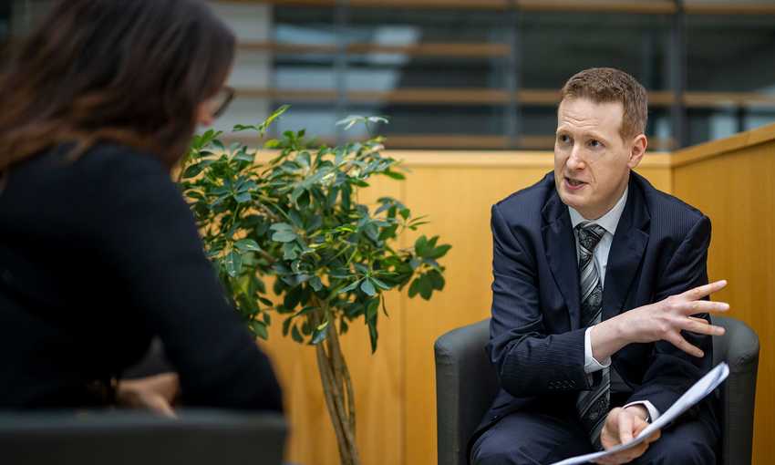 A man dressed in a suit converses with a woman, showcasing a professional dialogue between the two.