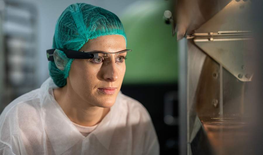 A woman wearing a green hair net, and using a single eye magnifying glass as she works
