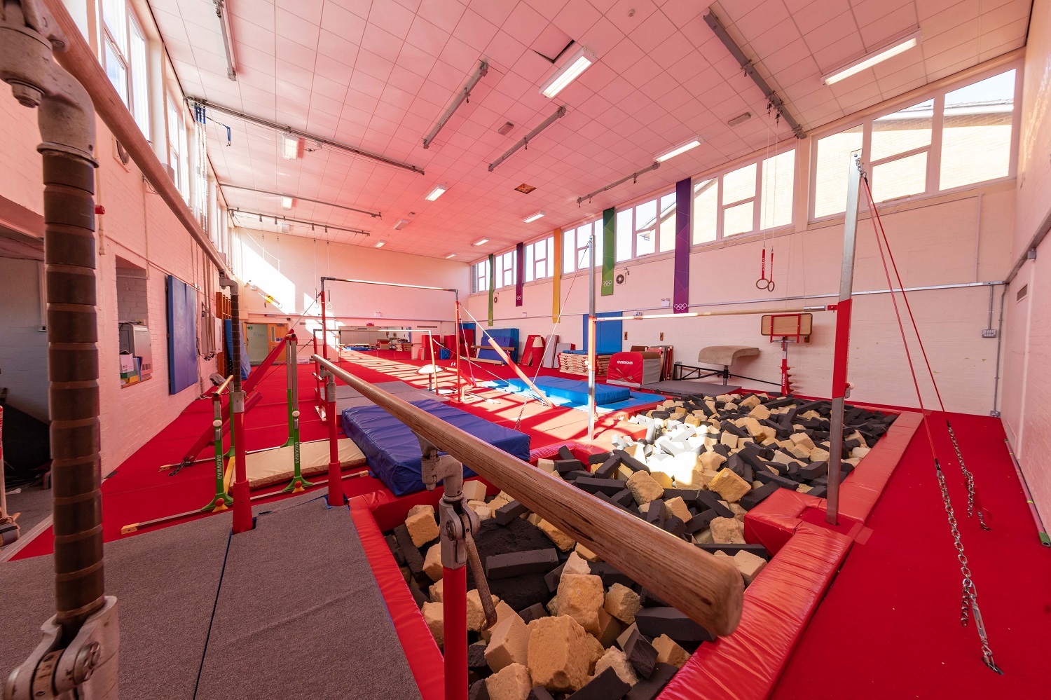 A colourful gymnasium featuring several balance beams, mats and soft landing pits