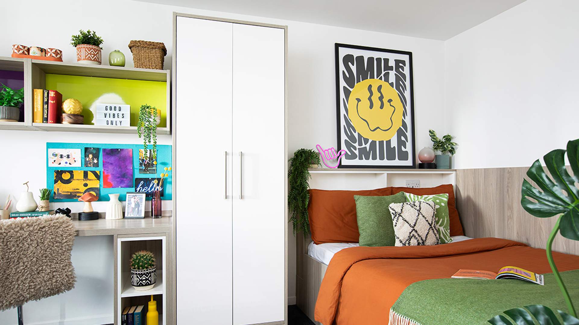 A cozy bedroom featuring a bed, a desk, and a green plant in the corner, creating a serene atmosphere.