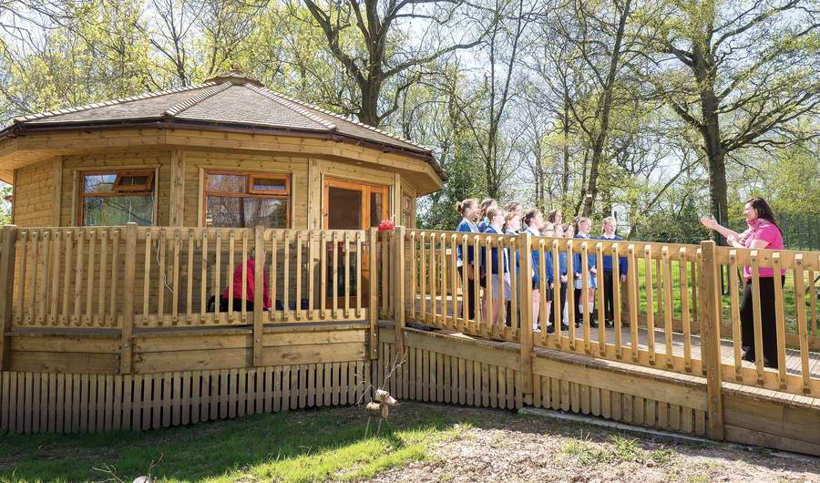 A group of children stand on a walkway leading to a small wooden building.