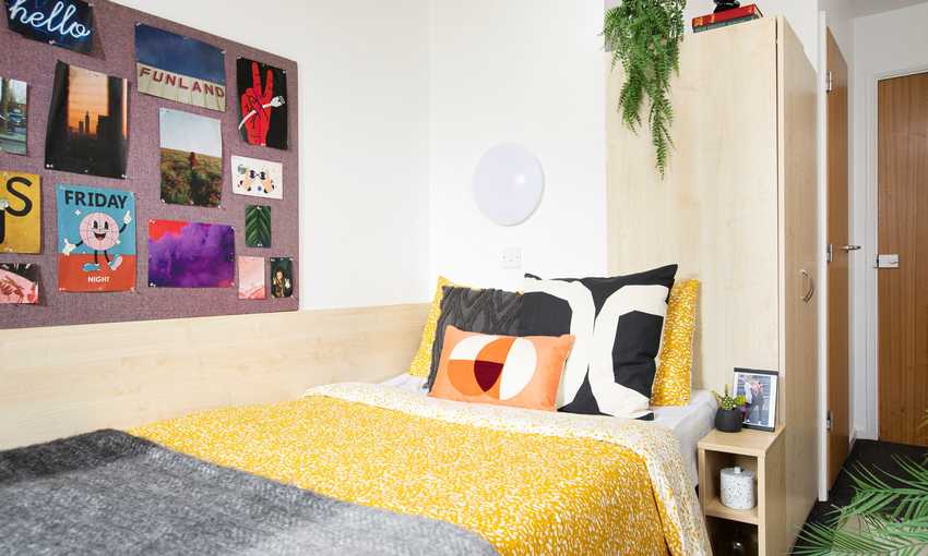 A decorated bedroom complete with posters hanging on a display board and made up bed