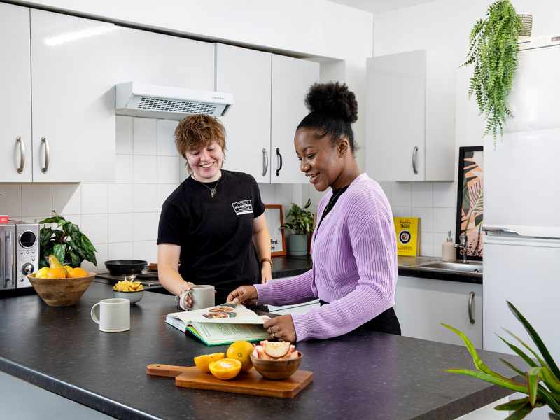 Two young women read a cookbook on a large kitchen island in Clodien House accommodation