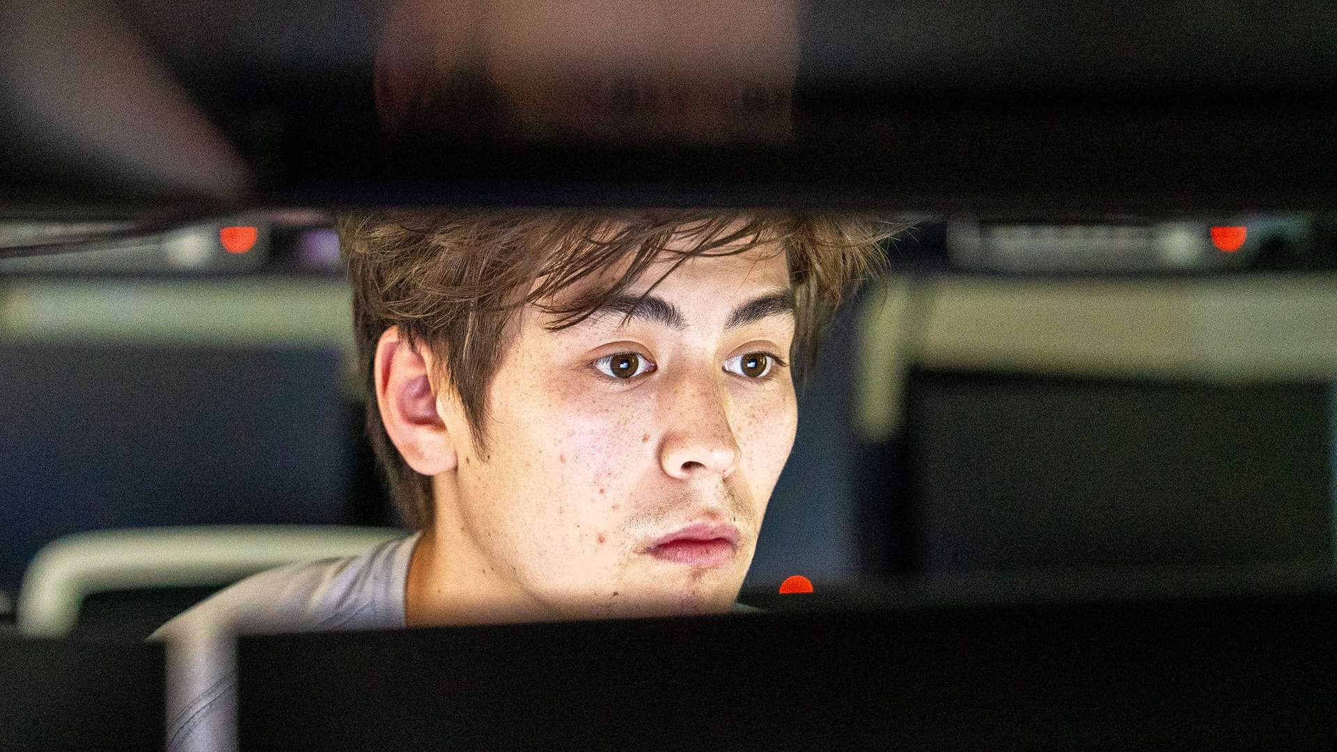 A close-up of a person looking at a computer monitor. Their face is lit from the light of the screen.