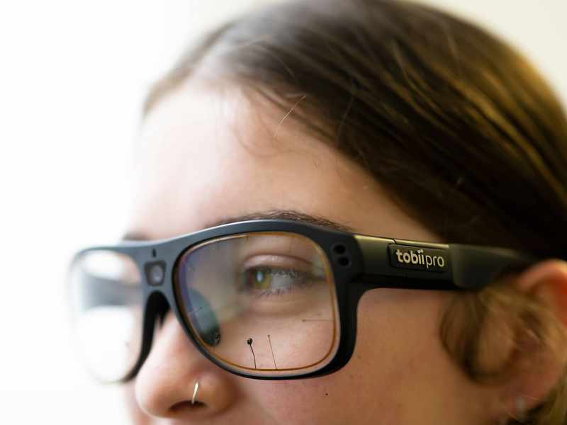 A close-up of a person wearing thick glasses. The glasses appear to have sensors on the front.