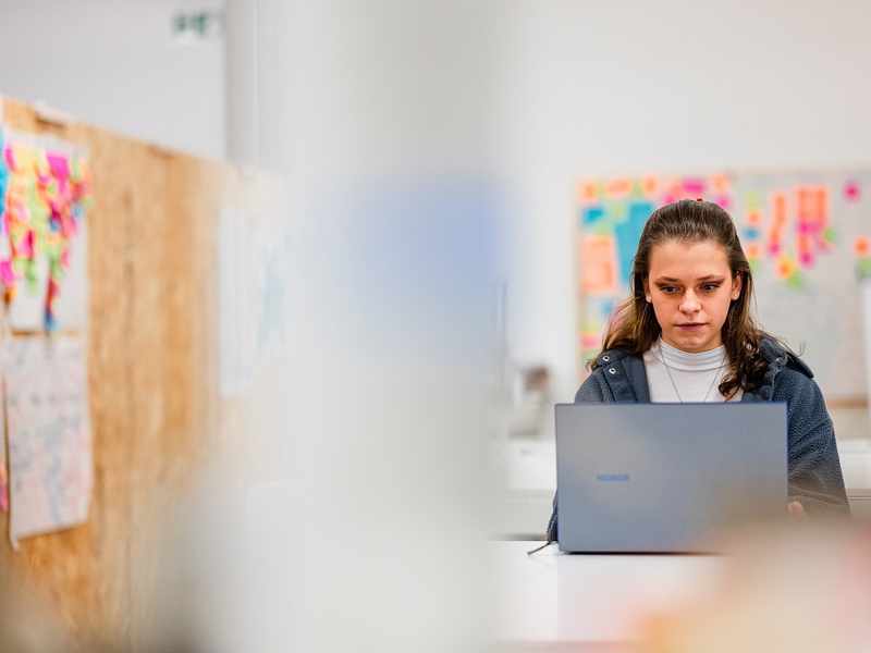 A young adult works from a laptop in an arts workspace