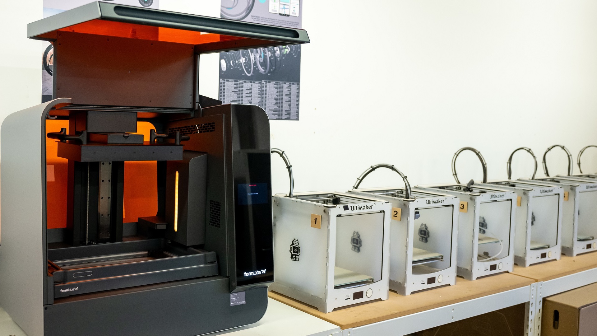 A collection of 3D Printers lined up on a row of desks
