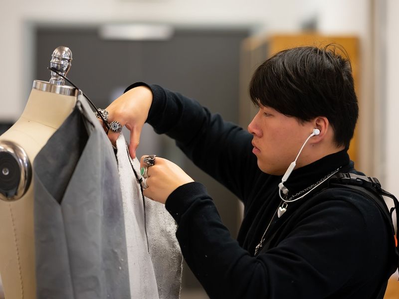 A young adult adjusts a piece of fabric dressed on a mannequin