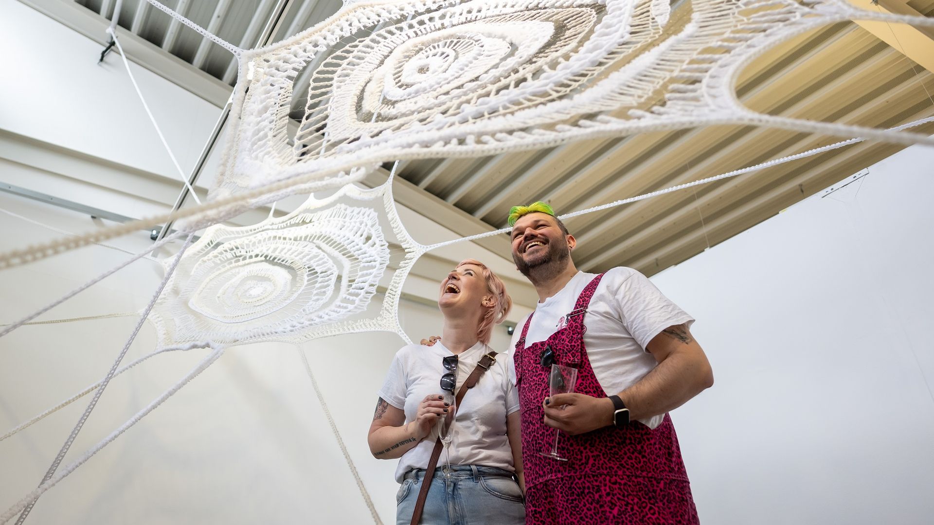 Two young adults stand underneath a large spiderweb art installation