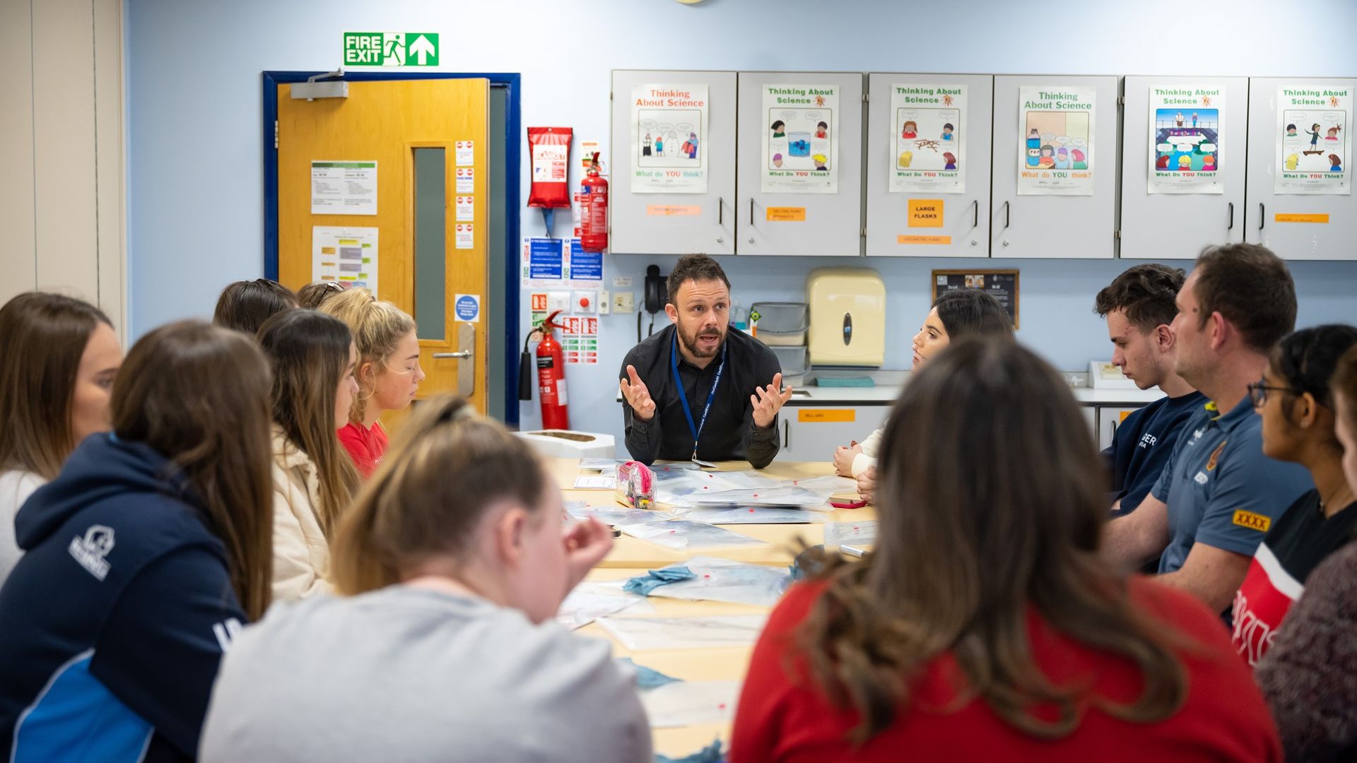 Teacher speaks to group of pupils around a classroom table