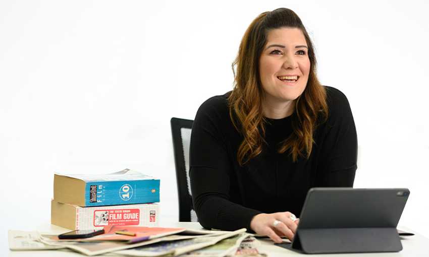 Lecturer sitting at a desk filled with books, papers, and an electronic tablet