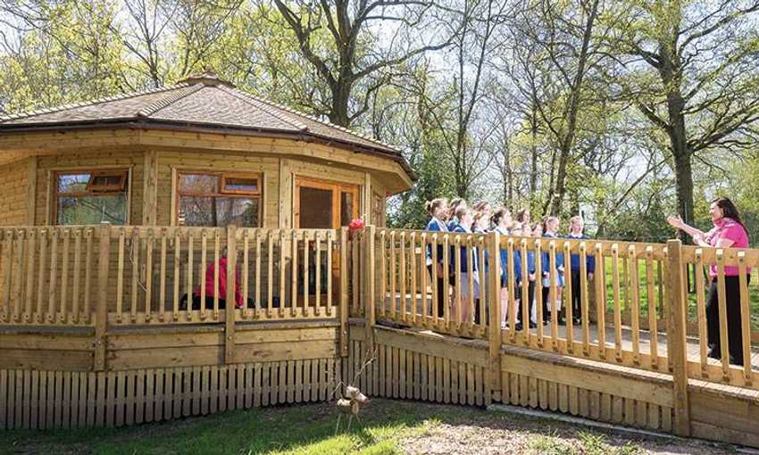 Pupils stand in front of wooden cabin with surrounding wooden veranda and disability ramp