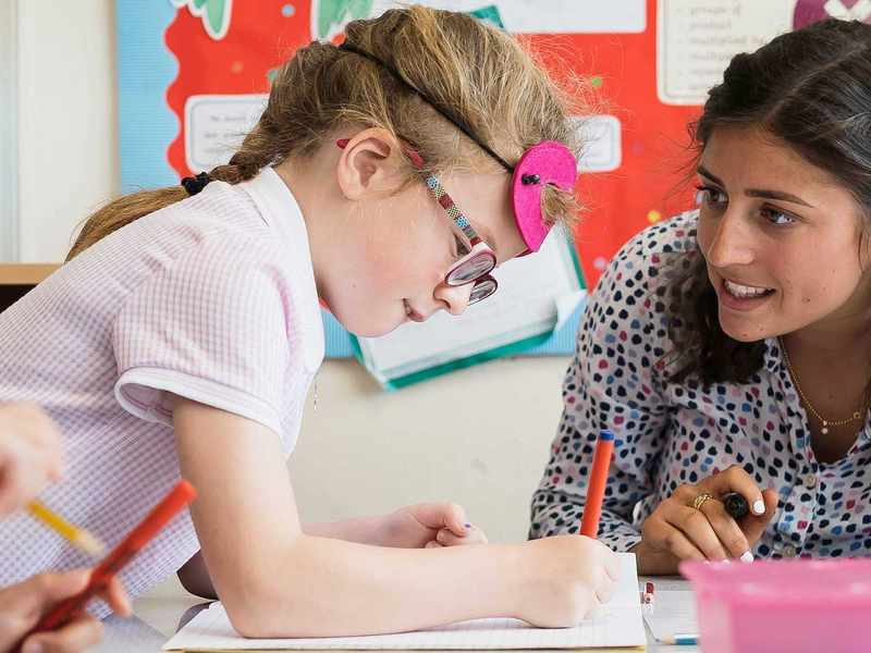 Teacher talks with young pupil as they write with a pen