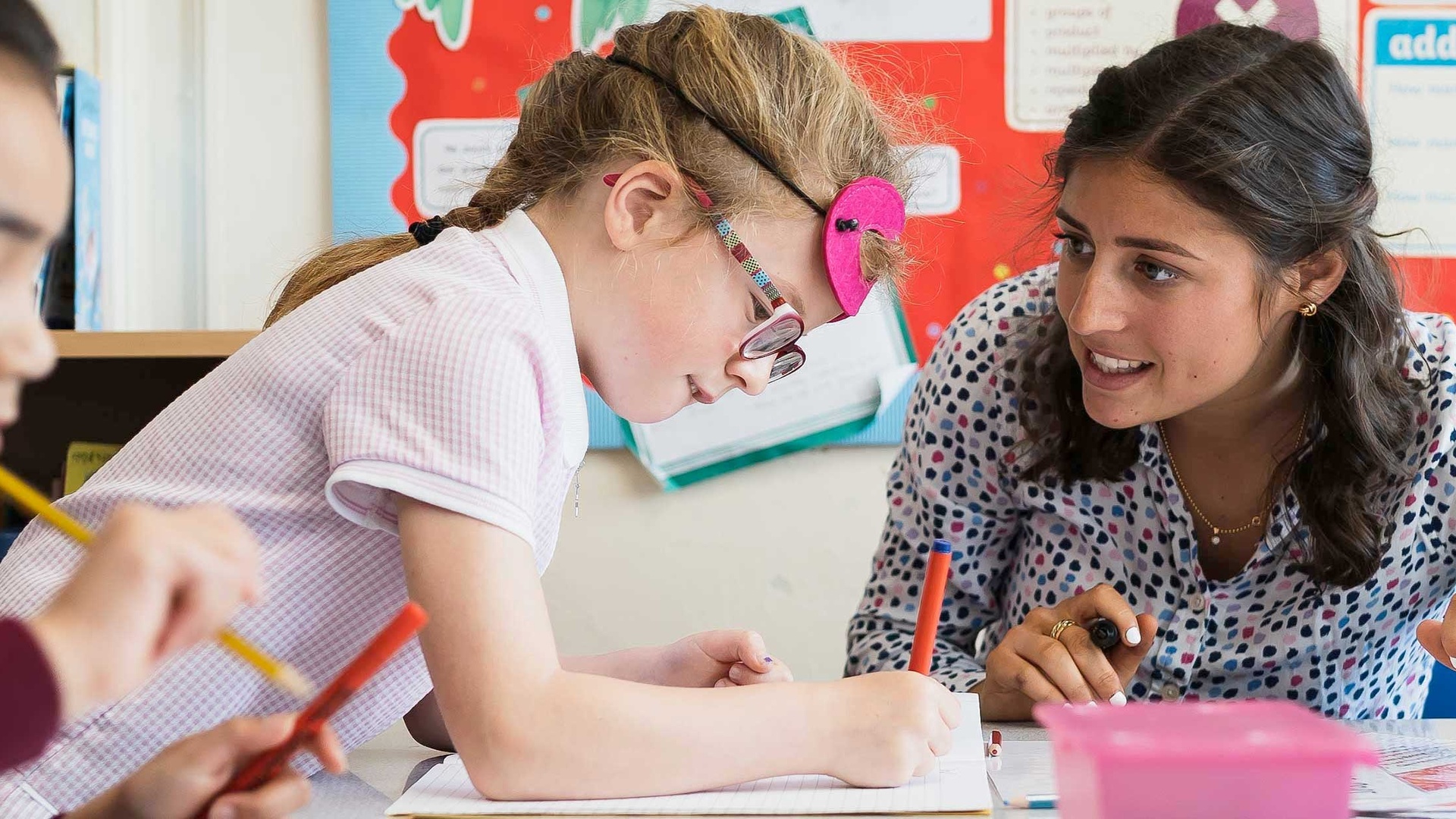 Teacher talks with young pupil as they write with a pen