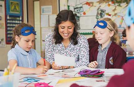 Teacher sits with students as they look at a piece of paper