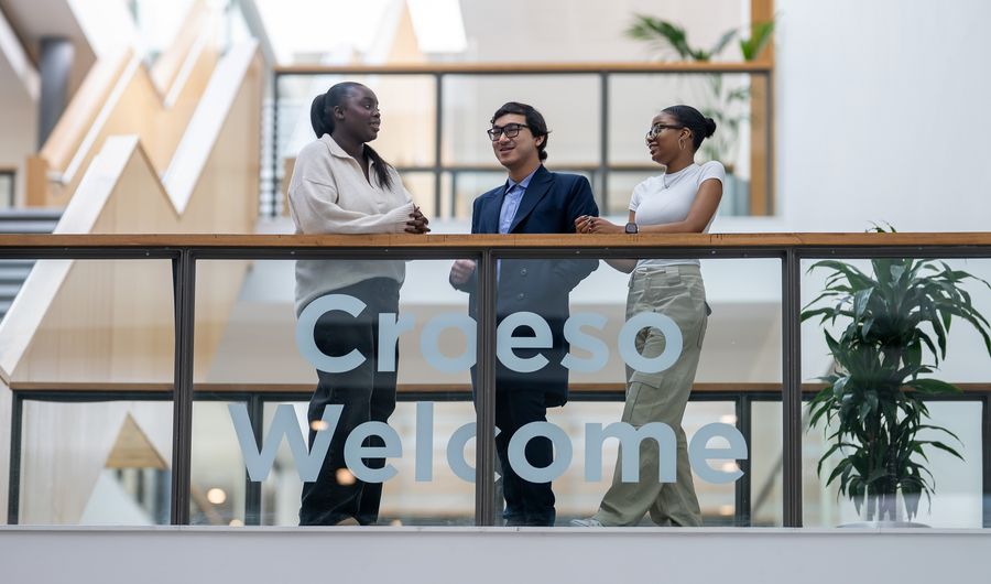 Three students stand talking together on a second floor mezzanine in the Cardiff School of Management building