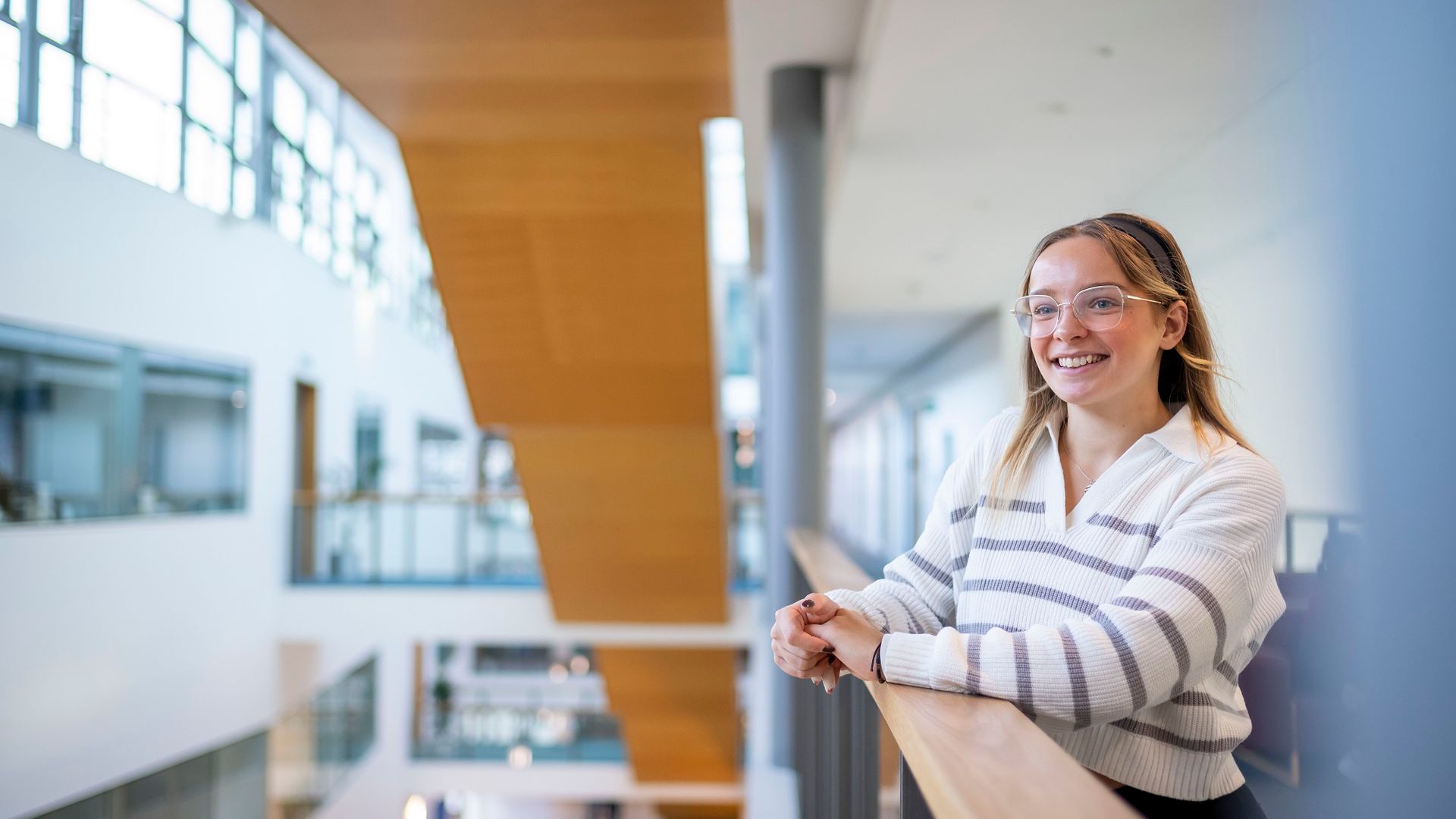 A young woman leans on the railing of a mezzanine in the Cardiff School of Management
