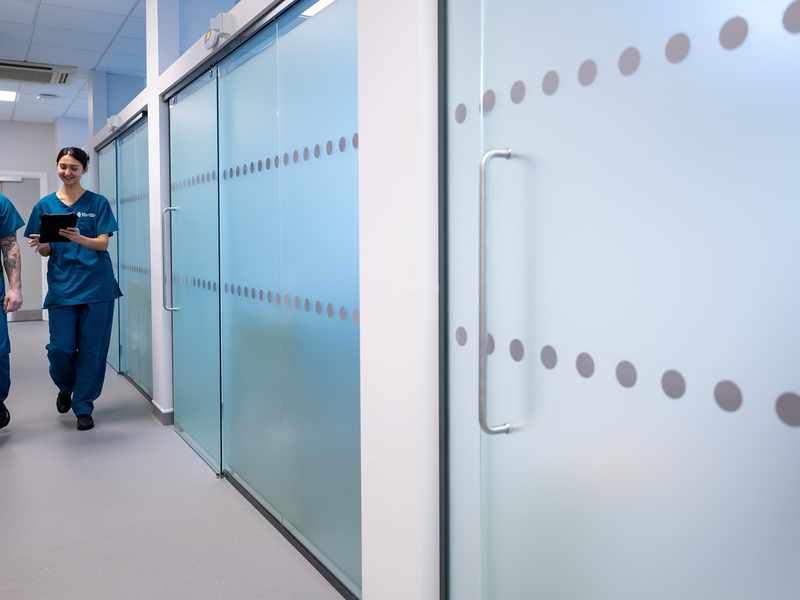 Two young adults in blue nursing scrubs walk through a corridor