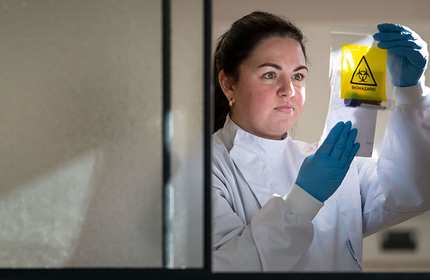 Student in white overalls and blue gloves holds up and reads from a piece of paper