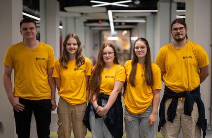 Five young adults in matching yellow t-shirts stand in a line