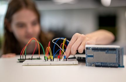 A young adult places a wire into a board of colourful wires