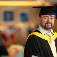 A man wearing a graduation gown and cap, celebrating his academic achievement with a proud smile.
