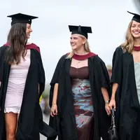 Three women in graduation gowns walking together, celebrating their academic achievements with smiles and camaraderie.