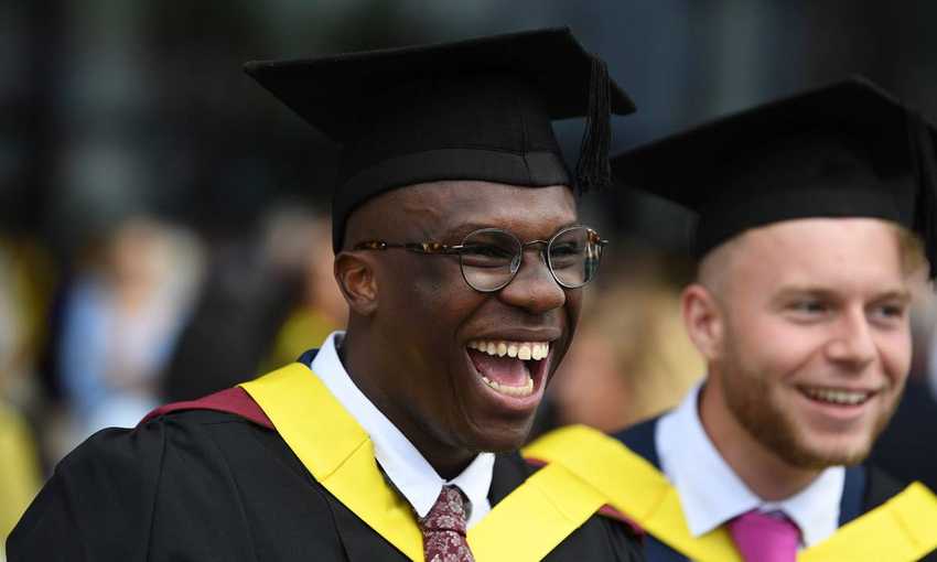 Cardiff Met student, wearing a graduate cap and gown, laughing with an open mouth