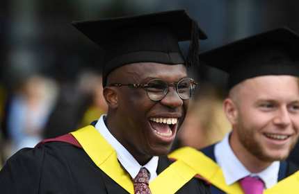 Cardiff Met student, wearing a graduate cap and gown, laughing with an open mouth