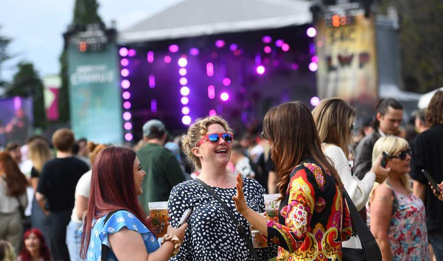 A group of people engaged in conversation at an outdoor music festival, surrounded by colourful decorations and a lively atmosphere.